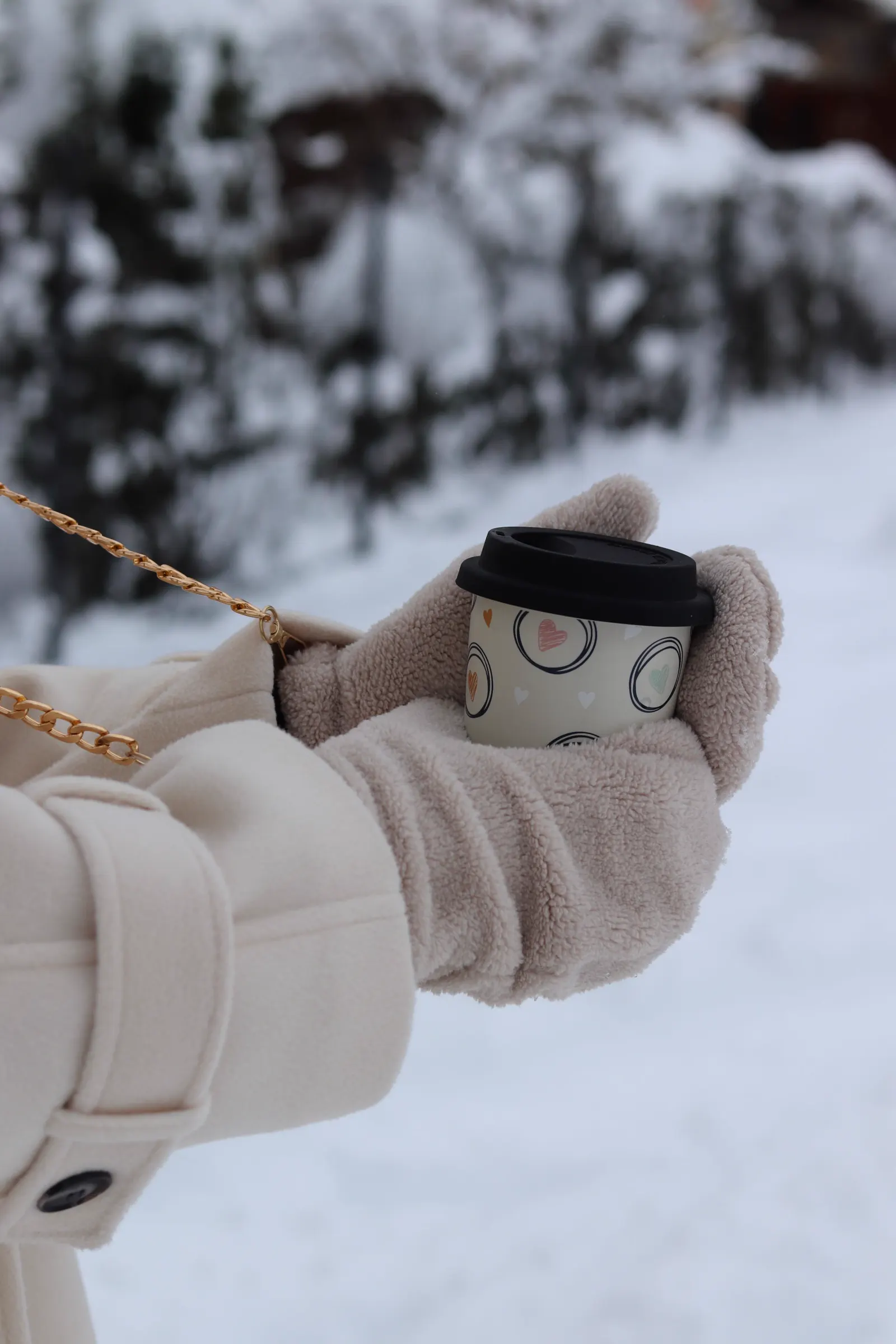 Mittened hands holding a warm cup in the snow